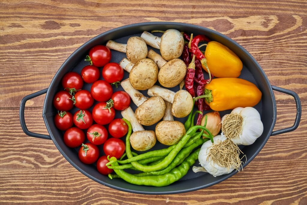 A top-down view of fresh vegetables including tomatoes, mushrooms, peppers, and garlic in a circular pan.