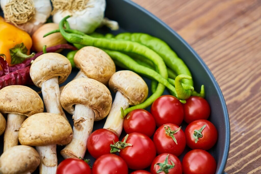 A close-up of various fresh vegetables and mushrooms in a pan on a wooden surface.