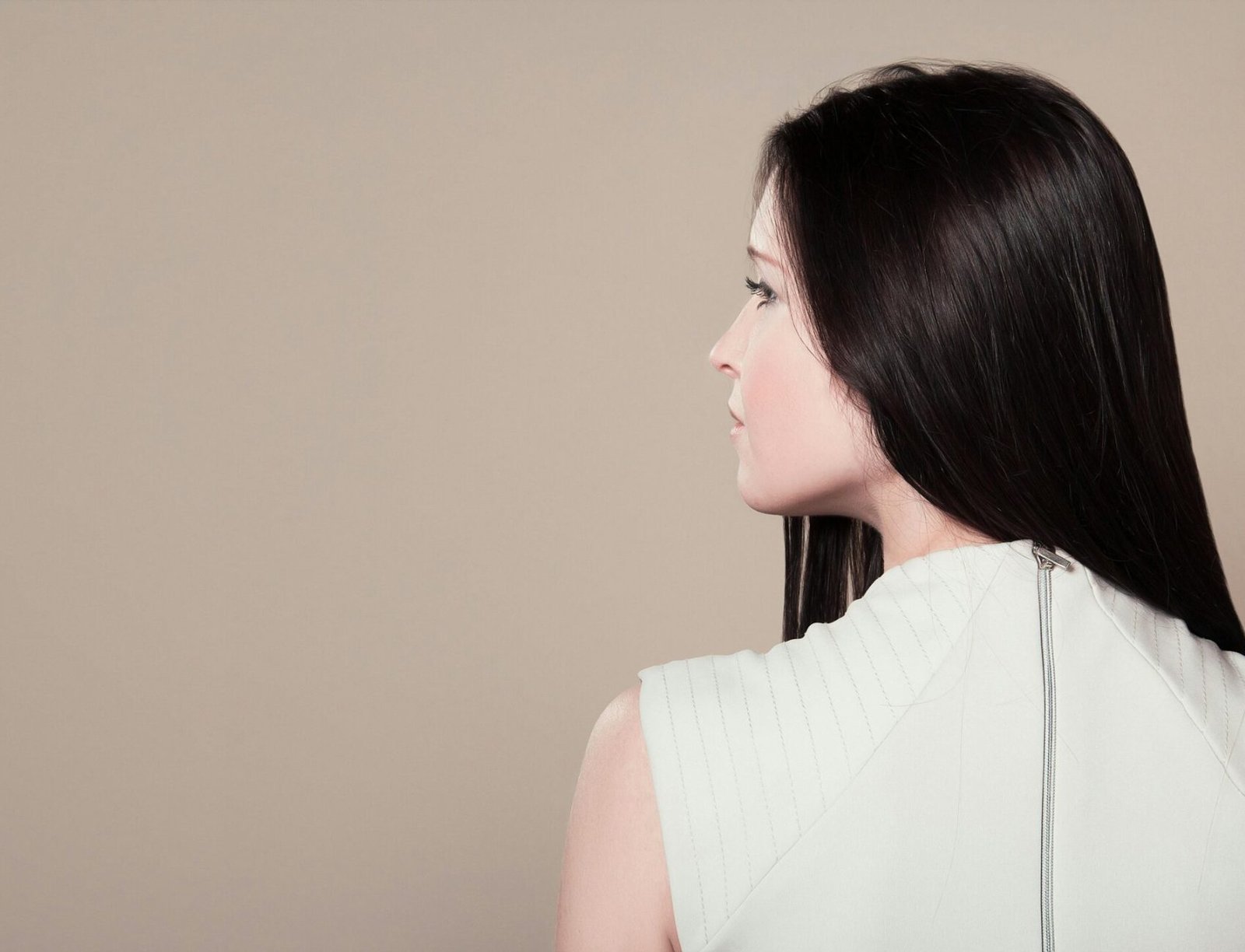 Profile view of a brunette woman in white attire indoors on a neutral background.