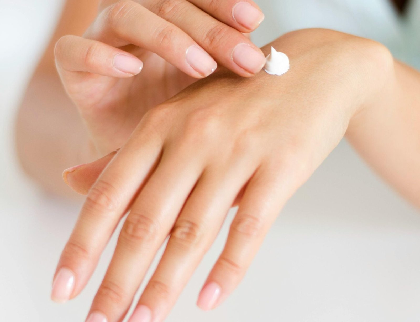 A woman applying cream on her hands, highlighting skincare and self-care concepts.